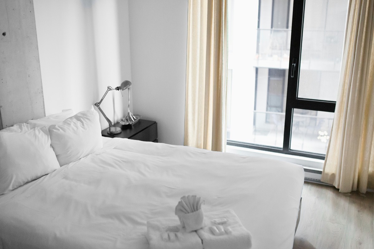 Clean furnished bedroom with a made bed, nightstand lamp, and daylit window